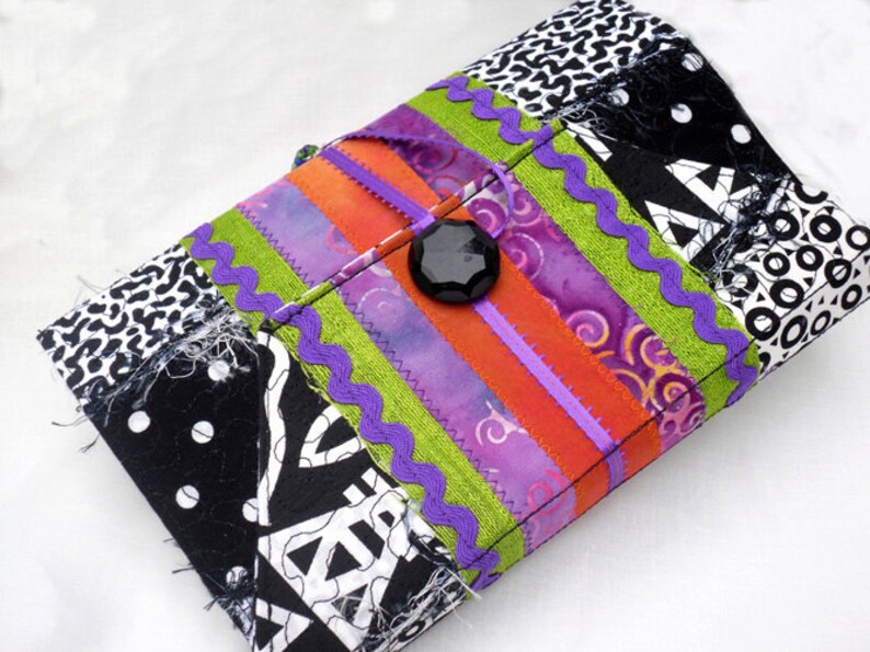 May include: A black and white patchwork fabric clutch with a purple, green, and orange striped design. A black button is in the center of the clutch.