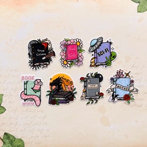 May include: Eight colourful stickers with book-themed designs. Titles include "True Crime," "Book Girly," "Sci-Fi," "Book Worm," "Dark Romance," and "Fantasy." Each sticker features unique illustrations and text, perfect for book lovers.