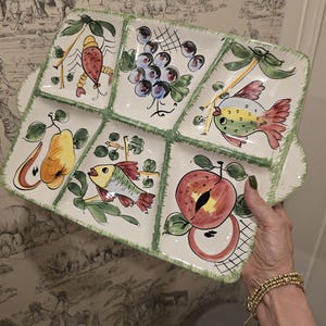 May include: A rectangular ceramic serving tray with five divided sections, featuring hand-painted illustrations of a lobster, grapes, two fish, a pear, and a peach. The tray has a cream-coloured base with green sponged edges and integrated handles.