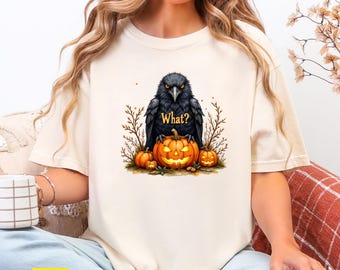May include: Ivory-colored t-shirt featuring a Halloween-themed graphic. The design includes a black crow with the word "What?" and a collection of orange pumpkins. The shirt is a comfortable, casual style.