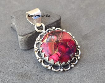 May include: A silver pendant featuring a large, round, red and purple stone. The stone is set in a decorative silver frame with a scalloped edge. The pendant has a silver bail for a chain. The text "DevJewelsIndia" is visible.