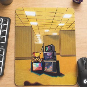 Puede incluir: Una alfombrilla de ratón rectangular con una ilustración gráfica de un oso amarillo sentado entre una pila de televisores antiguos. El fondo muestra una habitación de paredes amarillas con techo de rejilla y una silueta oscura a lo lejos.