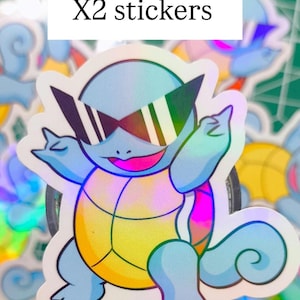 Peut inclure: Autocollant holographique représentant une tortue de dessin animé portant des lunettes de soleil. La tortue est bleu clair avec une carapace jaune et une bouche rose. Le texte "X2 stickers" est dans un rectangle blanc.