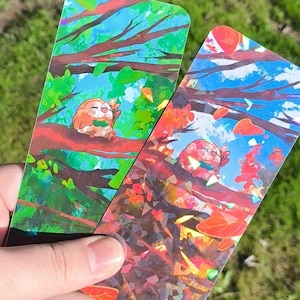 May include: Two colorful bookmarks featuring a cartoon owl perched on a tree branch. One bookmark has a green and blue background, the other has a red and blue background. The artist's name, NESOR.ART, is printed on the bottom of one bookmark.