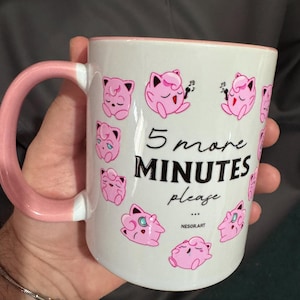 Puede incluir: Una taza de cerámica blanca con asa y borde rosa, que presenta un patrón repetitivo de personajes de dibujos animados rosas. El texto "5 more MINUTES please..." está impreso en negro, con "NESOR.ART" escrito en letras negras pequeñas.