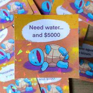 Può includere: Adesivo quadrato con un'illustrazione di Squirtle in blu e beige, sdraiato sulla schiena. L'adesivo ha il testo "Need water... and $5000" in un ovale bianco. Lo sfondo è arancione con accenti olografici.