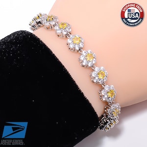 May include: A silver-toned bracelet featuring a series of connected flower-shaped links. Each link consists of a central round yellow stone surrounded by a halo of small, clear, sparkling white stones set in a metallic frame.