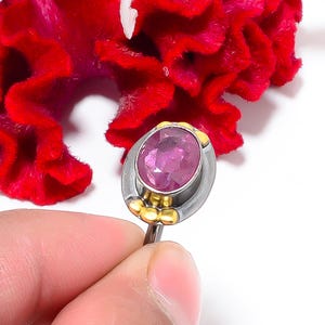 Peut inclure: Bague en argent orn&eacute;e d'une grosse pierre rose ovale. La bague pr&eacute;sente des d&eacute;tails dor&eacute;s autour de la pierre et sur le corps. Une fleur rouge vif sert de fond.