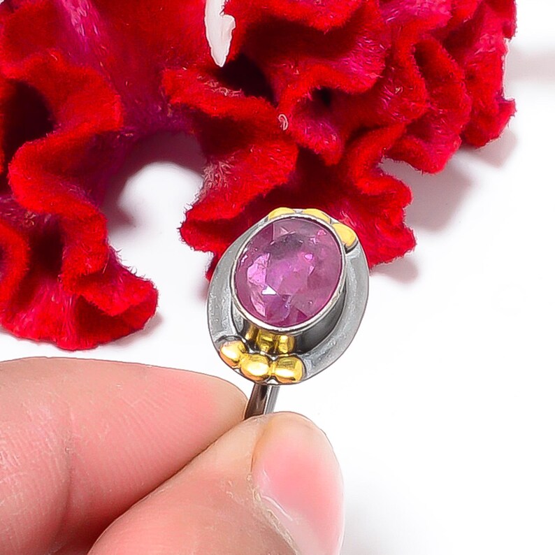 Peut inclure: Bague en argent orn&eacute;e d'une grosse pierre rose ovale. La bague pr&eacute;sente des d&eacute;tails dor&eacute;s autour de la pierre et sur le corps. Une fleur rouge vif sert de fond.