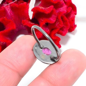 Peut inclure: Bague en argent avec une pierre pr&eacute;cieuse rose de forme ovale. La bague a un anneau simple et un petit poin&ccedil;on rond. Le fond pr&eacute;sente un &eacute;l&eacute;ment floral rouge vif.
