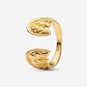 May include: A gold-colored open ring with a textured, wing-like design. The ring features a split shank and a detailed pattern resembling feathers or scales. The ring is made of a shiny, polished metal.