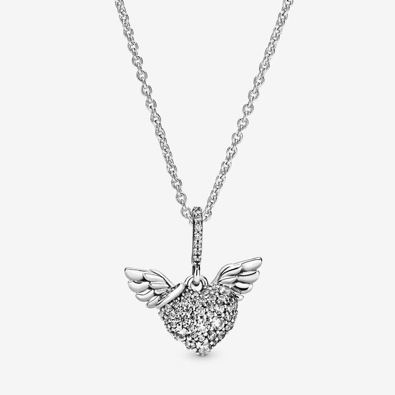 May include: A silver necklace featuring a heart-shaped pendant with sparkling stones and small wings. The pendant hangs from a delicate chain, creating a romantic and elegant accessory.