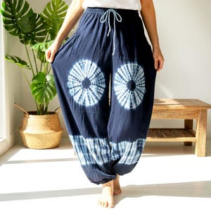 May include: Navy blue tie-dye pants with a drawstring waist. The pants feature large, circular white and blue tie-dye patterns on the front. The loose-fitting pants are made of a soft, flowing fabric, perfect for casual wear.