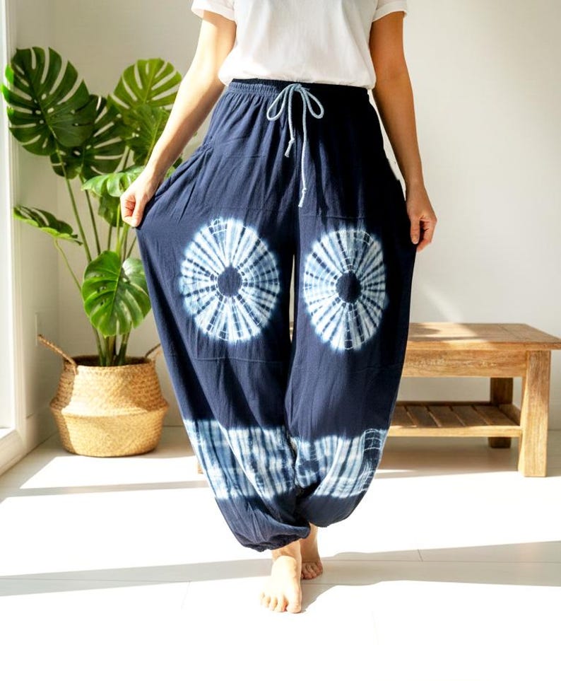 May include: Navy blue tie-dye pants with a drawstring waist. The pants feature large, circular white and blue tie-dye patterns on the front. The loose-fitting pants are made of a soft, flowing fabric, perfect for casual wear.