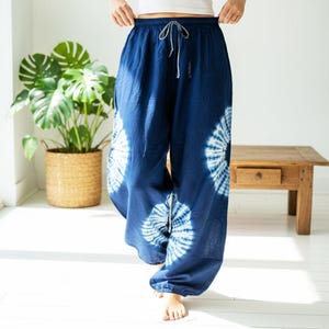 May include: Navy blue tie-dye pants with a drawstring waist. The pants feature white circular patterns and are made of a lightweight fabric. The model is wearing a white tank top. The pants are a relaxed fit.