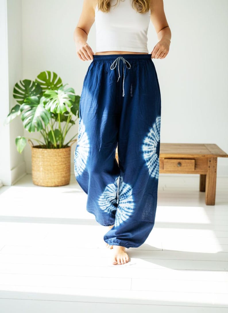 May include: Navy blue tie-dye pants with a drawstring waist. The pants feature white circular patterns and are made of a lightweight fabric. The model is wearing a white tank top. The pants are a relaxed fit.
