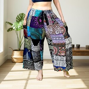 Op de afbeelding: Wijdvallende broek met een levendig patchworkontwerp met ingewikkelde mandala- en paisley-patronen in tinten blauw, paars, zwart en wit. Deze losvallende broek heeft een elastische tailleband en twee zijzakken.