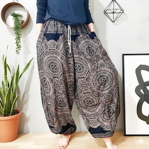 Op de afbeelding: Losvallende, wijde broek met een donker marineblauwe basis en een ingewikkeld, herhalend wit cirkelvormig patroon in mandala-stijl. De broek is voorzien van een elastische tailleband met een wit trekkoord en zijzakken.