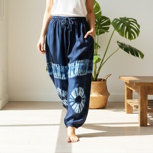 May include: Navy blue tie-dye pants with a drawstring waist and pockets. The pants feature a unique pattern of white and blue tie-dye designs. The loose-fitting pants are made of a soft, flowing fabric, perfect for casual wear.