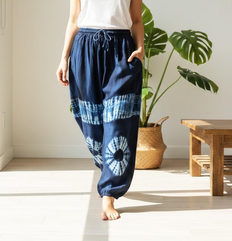 May include: Navy blue tie-dye pants with a drawstring waist and pockets. The pants feature a unique pattern of white and blue tie-dye designs. The loose-fitting pants are made of a soft, flowing fabric, perfect for casual wear.
