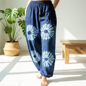May include: Dark blue tie-dye pants with a drawstring waist and white circular patterns. The loose-fitting pants are made of a soft fabric. The pants are part of a casual clothing collection.