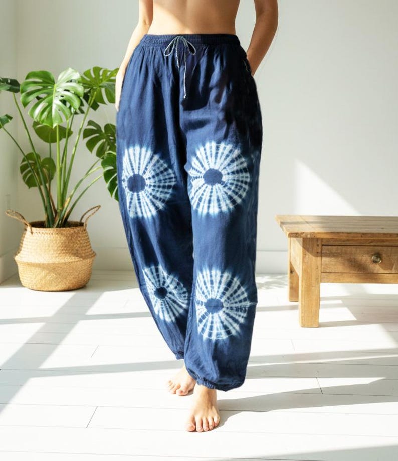 May include: Dark blue tie-dye pants with a drawstring waist and white circular patterns. The loose-fitting pants are made of a soft fabric. The pants are part of a casual clothing collection.