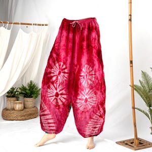 May include: Red tie-dye pants with a drawstring waist and pockets. The pants feature a white floral pattern and a loose, comfortable fit. These bohemian-style pants are perfect for casual wear.