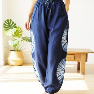 May include: Navy blue tie-dye pants with a drawstring waist and pockets. The pants feature a white circular tie-dye pattern on the lower legs. The loose-fitting pants are made of a soft, flowing fabric, perfect for casual wear.