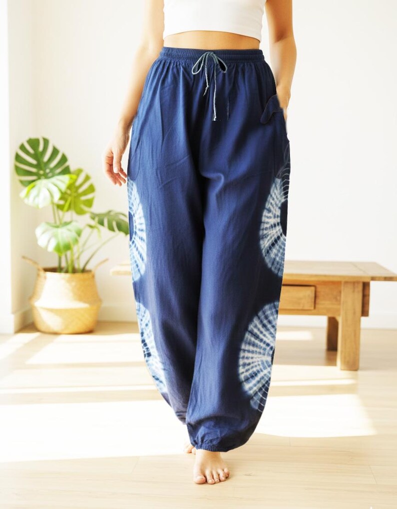 May include: Navy blue tie-dye pants with a drawstring waist and pockets. The pants feature a white circular tie-dye pattern on the lower legs. The loose-fitting pants are made of a soft, flowing fabric, perfect for casual wear.