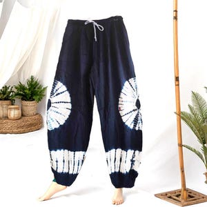 May include: Dark blue tie-dye pants with a white drawstring. The pants feature large white and blue circular patterns on the sides and white stripes at the ankles. The pants are made of a soft, flowing fabric.