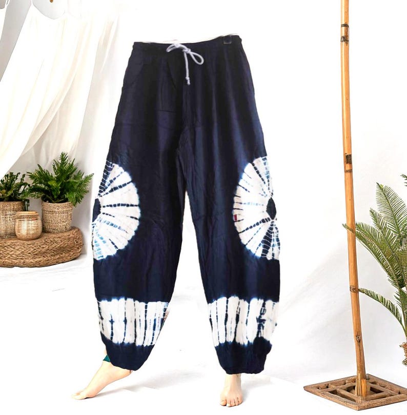 May include: Dark blue tie-dye pants with a white drawstring. The pants feature large white and blue circular patterns on the sides and white stripes at the ankles. The pants are made of a soft, flowing fabric.
