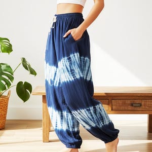 Könnte beinhalten: Marineblaue Hose mit Batikmuster, weißem Kordelzug in der Taille und Taschen. Die Hose hat eine lockere Passform und ist an den Knöcheln gebündelt. Das Batikmuster zeigt weiße Streifen auf dunkelblauem Hintergrund. Die Hose ist aus weichem Material.