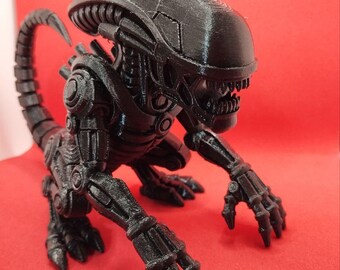 Puede incluir: Figura negra impresa en 3D de un Xenomorfo, criatura de la franquicia Alien. La figura está posada sobre una superficie roja, mostrando su detallado exoesqueleto, cabeza alargada y afilados dientes. La cola está curvada.