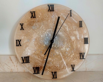 May include: A round wall clock with a cream-colored face, black Roman numerals, and black hands. The clock face has a swirling design with gold and silver glitter accents. The clock is a decorative home decor item.