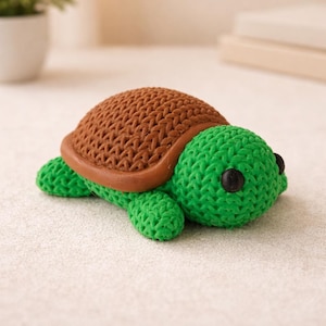 May include: A handmade turtle ornament with a textured brown shell and a green body. The turtle has black eyes and is made of a soft, possibly knitted, material. The ornament is a decorative item.
