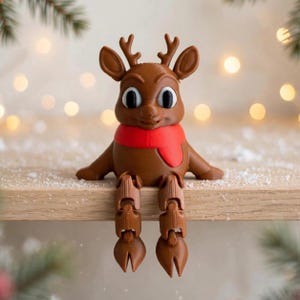 May include: A brown reindeer figurine with large black eyes and a bright red scarf wrapped around its neck. The reindeer has articulated legs that hang down, featuring detailed antlers and hooves, designed to sit on the edge of a flat surface.