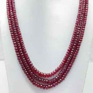May include: A multi-strand necklace of small, faceted, deep red beads. The necklace is displayed on a white mannequin bust, highlighting the layered design and the rich colour of the gemstone beads.