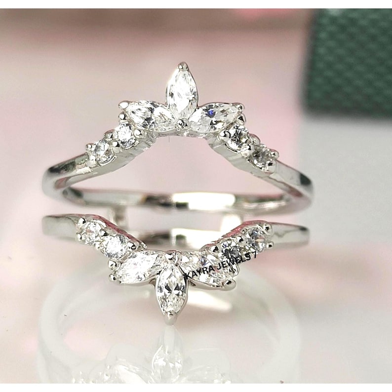 Puede incluir: Dos anillos plateados con piedras preciosas de talla marquesa y redonda. El anillo superior tiene un dise&ntilde;o floral con una piedra central de talla marquesa. El anillo inferior tiene un dise&ntilde;o similar. El texto "KAYRA JEWELS 7" es visible.