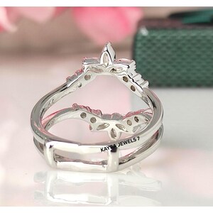 Puede incluir: Un anillo de plata con un dise&ntilde;o &uacute;nico. El anillo presenta una parte superior en forma de corona con un elemento central puntiagudo y peque&ntilde;os detalles decorativos. La banda tiene un dise&ntilde;o de doble capa. El texto "KAYRA JEWELS 7" es visible en el anillo.