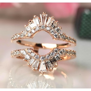 May include: Rose gold ring guard with a halo of baguette and round cut diamonds. The ring features a curved design with a row of small diamonds along the band. The top of the ring has a sunburst design with larger baguette diamonds.