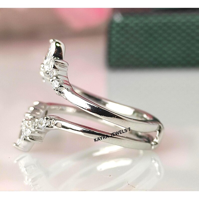 Puede incluir: Un anillo plateado con un dise&ntilde;o envolvente &uacute;nico. El anillo presenta peque&ntilde;as piedras preciosas transparentes a lo largo de la banda y en la parte superior. El texto "KAYRA JEWELS 7" es visible en el anillo.