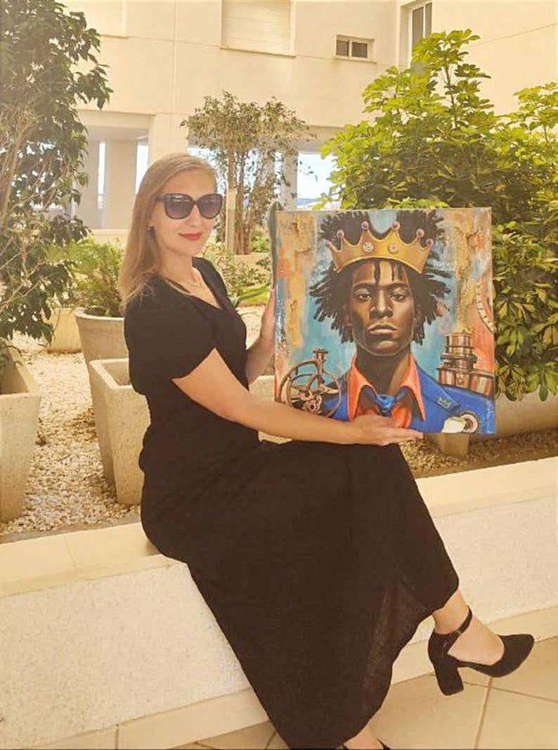 May include: An artwork featuring a portrait of a person wearing a gold crown, with a blue and orange background. The artwork is held by a person wearing a black dress and sunglasses.