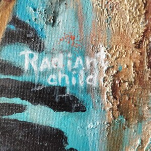 May include: Close-up of an abstract painting with textured brushstrokes. The artwork features a vibrant mix of colors, including turquoise, gold, and black. The words "Radiant child" are painted in white.