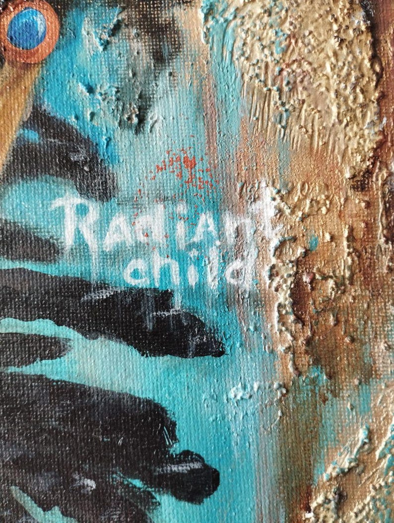 May include: Close-up of an abstract painting with textured brushstrokes. The artwork features a vibrant mix of colors, including turquoise, gold, and black. The words "Radiant child" are painted in white.