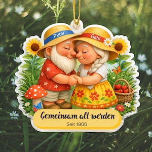 Puede incluir: Adorno decorativo con una pareja de dibujos animados, Peter y Gabi, abrazándose. Llevan sombreros de paja con cintas azules y rojas. El adorno incluye girasoles, una seta y una cesta de manzanas. El texto dice "Gemeinsam alt werden" y "Seit 1966".