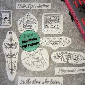 May include: A collection of black and white digital download PDF pattern stickers with various designs, including a cauldron, a sword, and the text "Hello, Feyre darling." A book with a red cover is partially visible in the background.