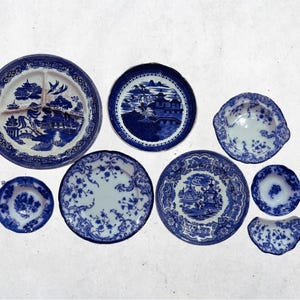 May include: A collection of blue and white porcelain plates and dishes. The plates feature various patterns, including floral designs and scenic landscapes. The arrangement includes plates of different sizes and shapes, showcasing a classic aesthetic.