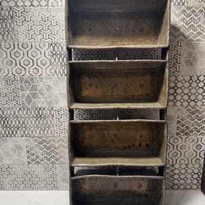 May include: A vintage, rectangular, metal shelf unit with five open compartments. The shelves are supported by a dark metal frame. The unit has a rustic, aged appearance, with visible wear and tear on the metal surface.