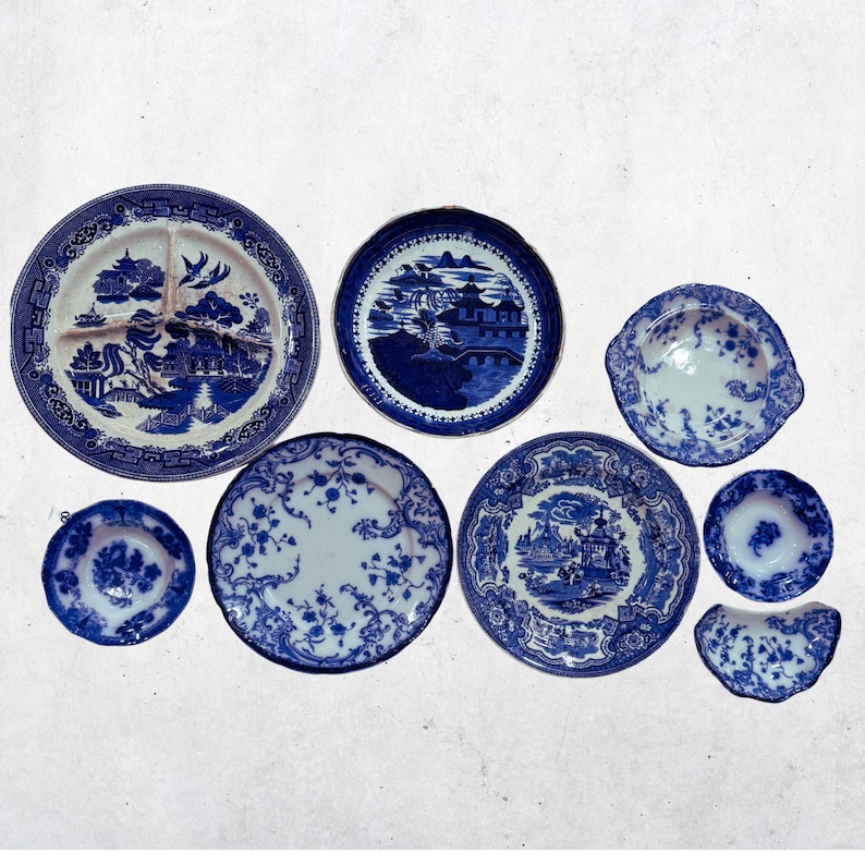 May include: A collection of blue and white ceramic plates with various patterns. The plates include a divided plate, a small bowl, and several round plates with floral and landscape designs. The collection is arranged on a white surface.
