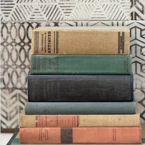 May include: A stack of antique books with various colors and textures. The books include titles like "The Complete Encyclopedia of Antiques," "Book of Marvels," and "American Painters." The spines display titles and author names.
